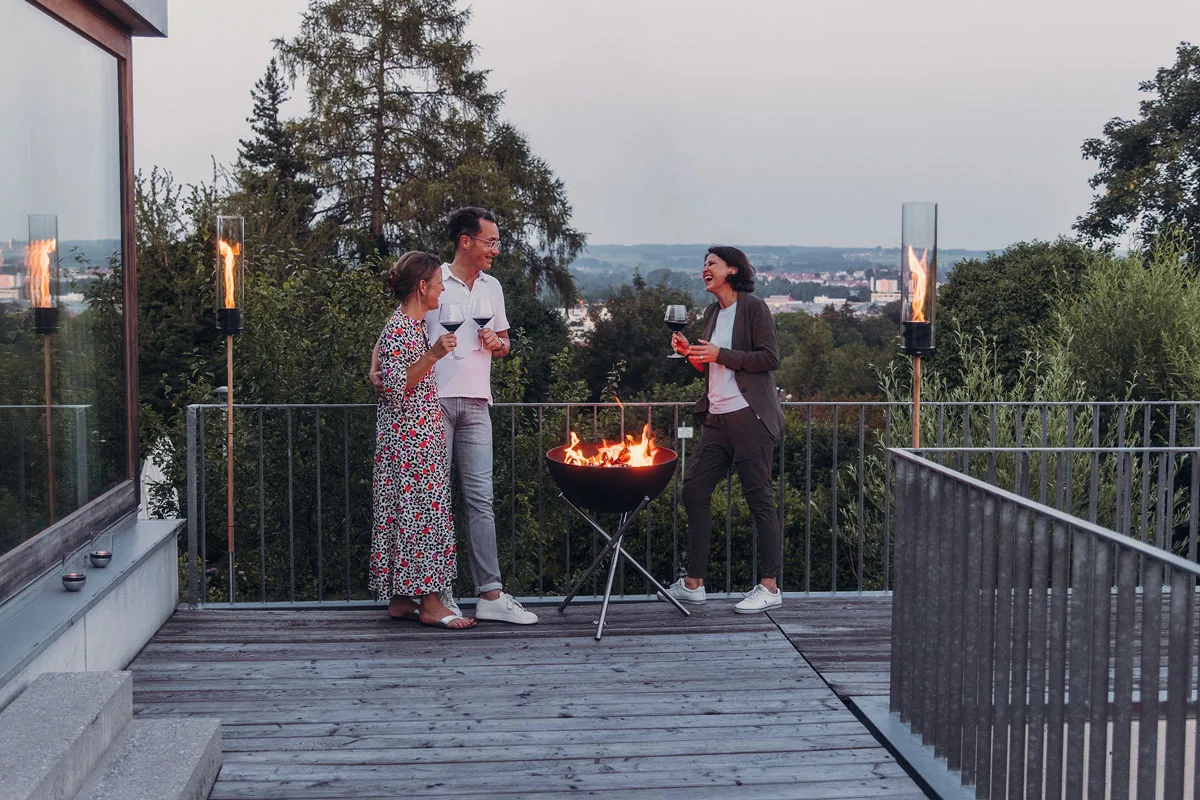 Brennende Feuerschale auf einer Terrasse, Gäste sitzen am Abend um das Feuer