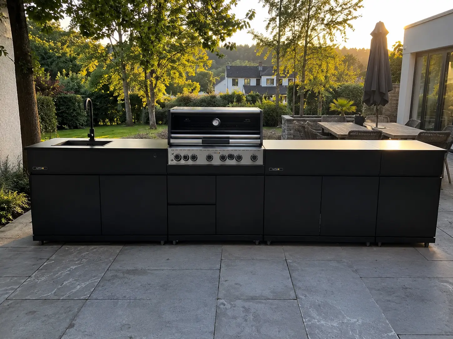 Schwarze Outta Outdoor-Küche in Linie mit Einbaugrill und Spüle auf einer Terrasse im Abendlicht